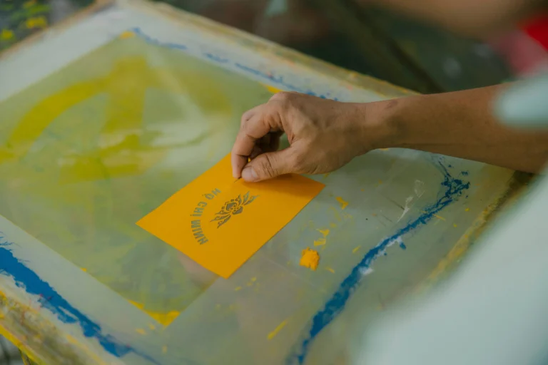 Screen printer inspecting the high-tension mesh on an aluminum pre-stretched screen printing frame in a workshop setting.